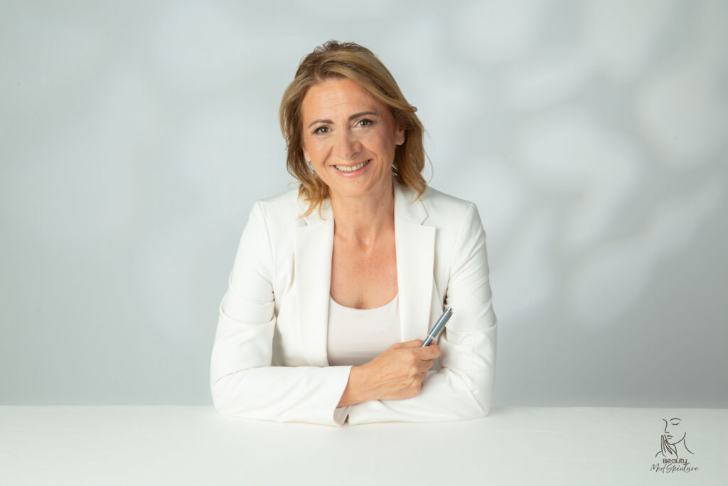 Tanja Vukas von Beauty MedSkinCare sitzt am Tisch und lächelt offen in die Kamera.